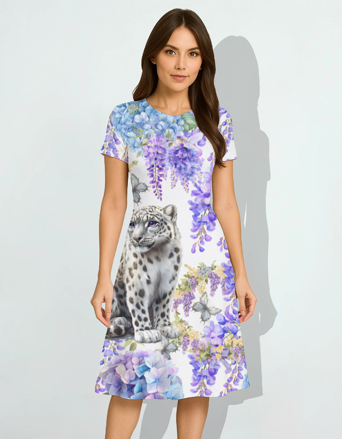 A woman wearing a short-sleeve dress featuring a colorful design of a snow leopard surrounded by purple flowers, standing against a light background.